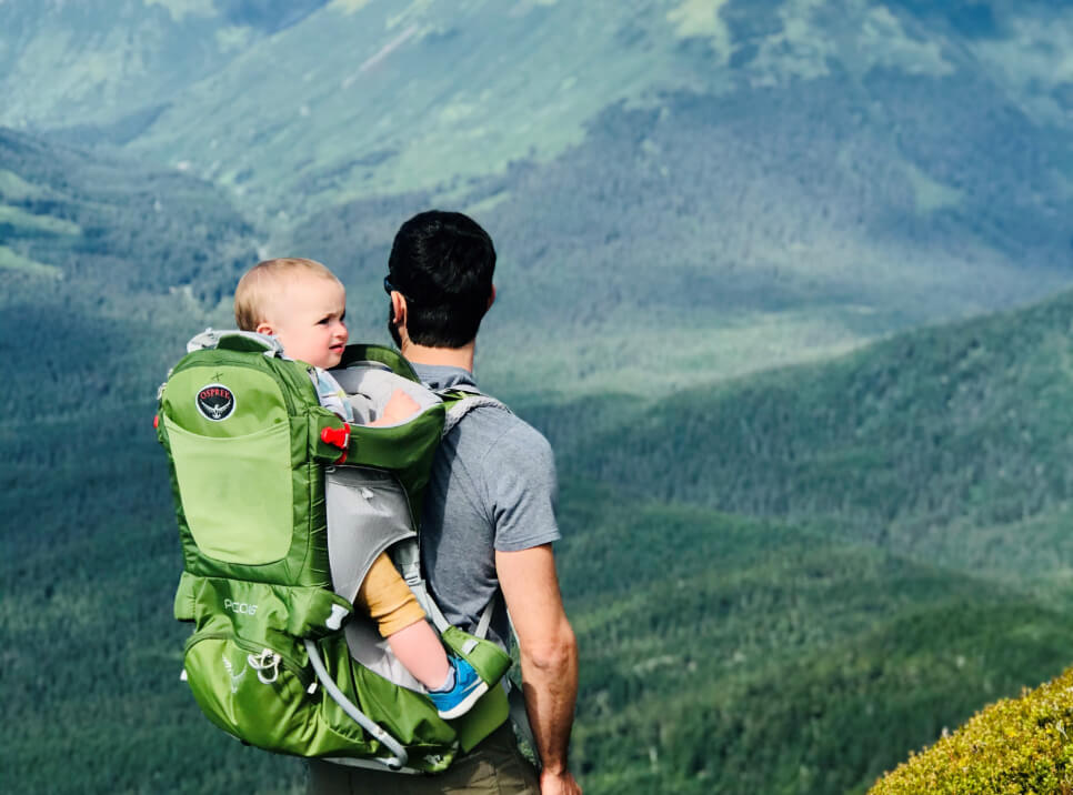 Dr. Gray hikes in Alaskan mountain with baby on his back